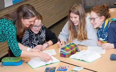 Eine Lehrerin hilft einer Gruppe von Schülerinnen bei ihren Aufgaben.