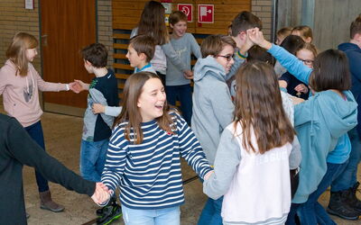 Eine Gruppe SchülerInnen hält sich an den Händen und lachen freudig gemeinsam.