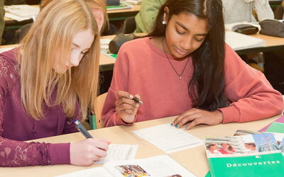 Zwei Schülerinnen arbeiten gemeinsam an einer Aufgabe in einem Klassenzimmer und konzentrieren sich auf ihre Aufgaben.