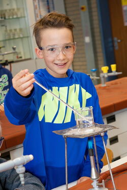 Ein Junge hält fröhlich ein Thermometer für ein Experiment.
