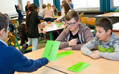 Eine Gruppe von SchülerInnen sitzt an einem Tisch und lernt mit grünen Papierkarten.