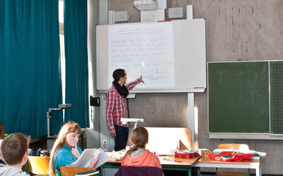 Ein Lehrer erklärt etwas am Whiteboard für eine Gruppe von aufmerksamen SchülerInnen.